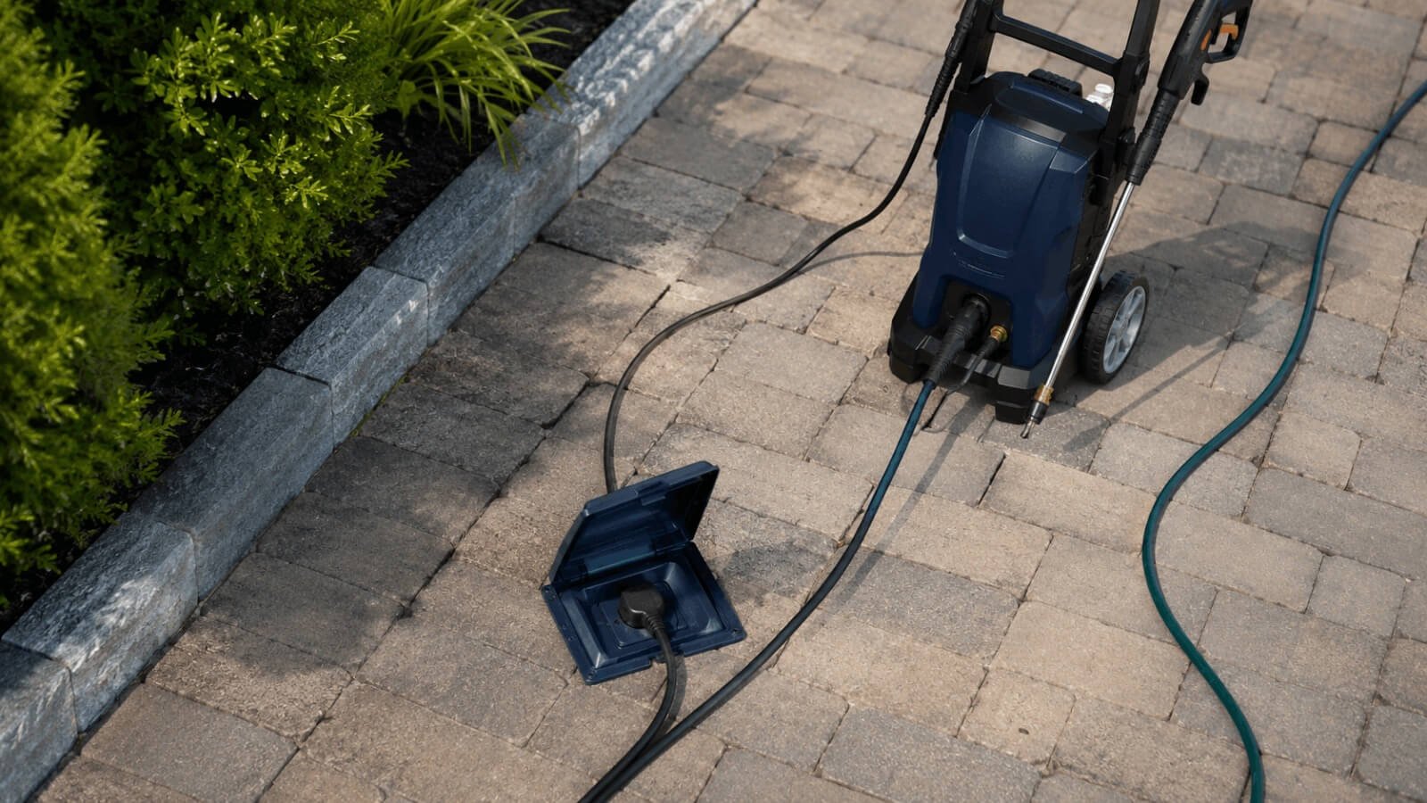 Close-up view of an electric pressure washer power cord connected to an outdoor covered outlet box